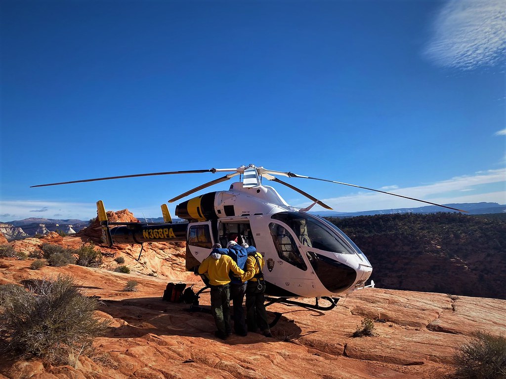 Two people help another into a helicopter parked on sandstone in a desert.